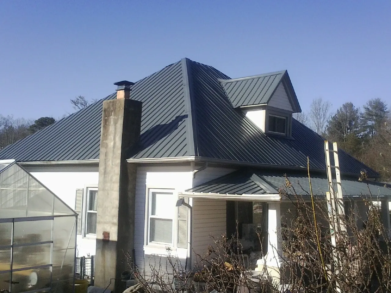 Dark blue standing seam metal roof on a white farmhouse with dormer — Slate & Tile Roof Repair by Roofing Brothers in Wausau