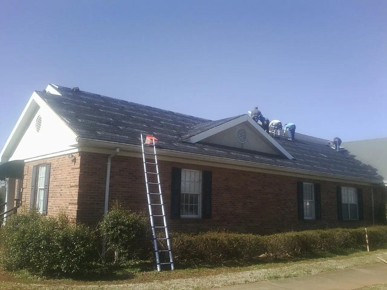 Crew tearing shingles off a brick ranch roof with a ladder set — Metal Roof Repair work by our crew in Wausau