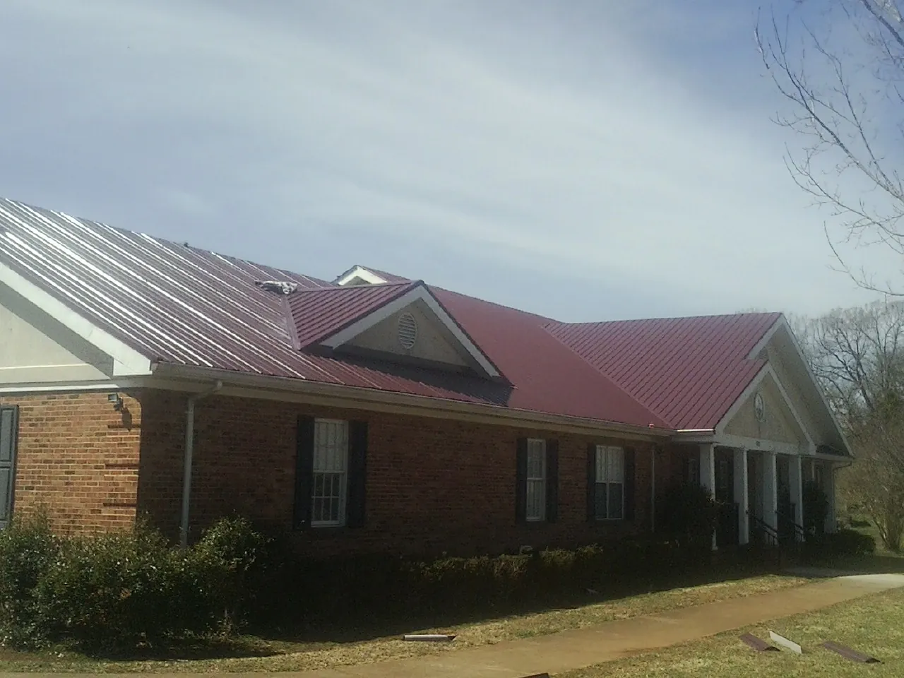 Red metal roof with gabled entries on a long brick building, from a Hail Damage Roof Repair job in Wausau