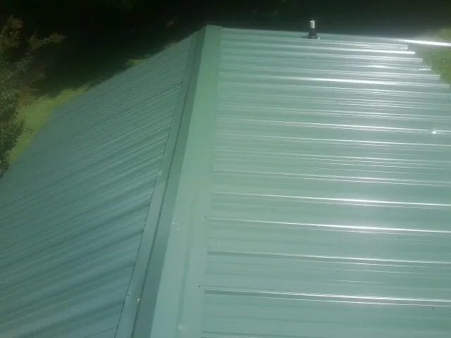 New green metal panels meeting at the ridge of a roof — Flat Roof Repair work by our crew in Wausau