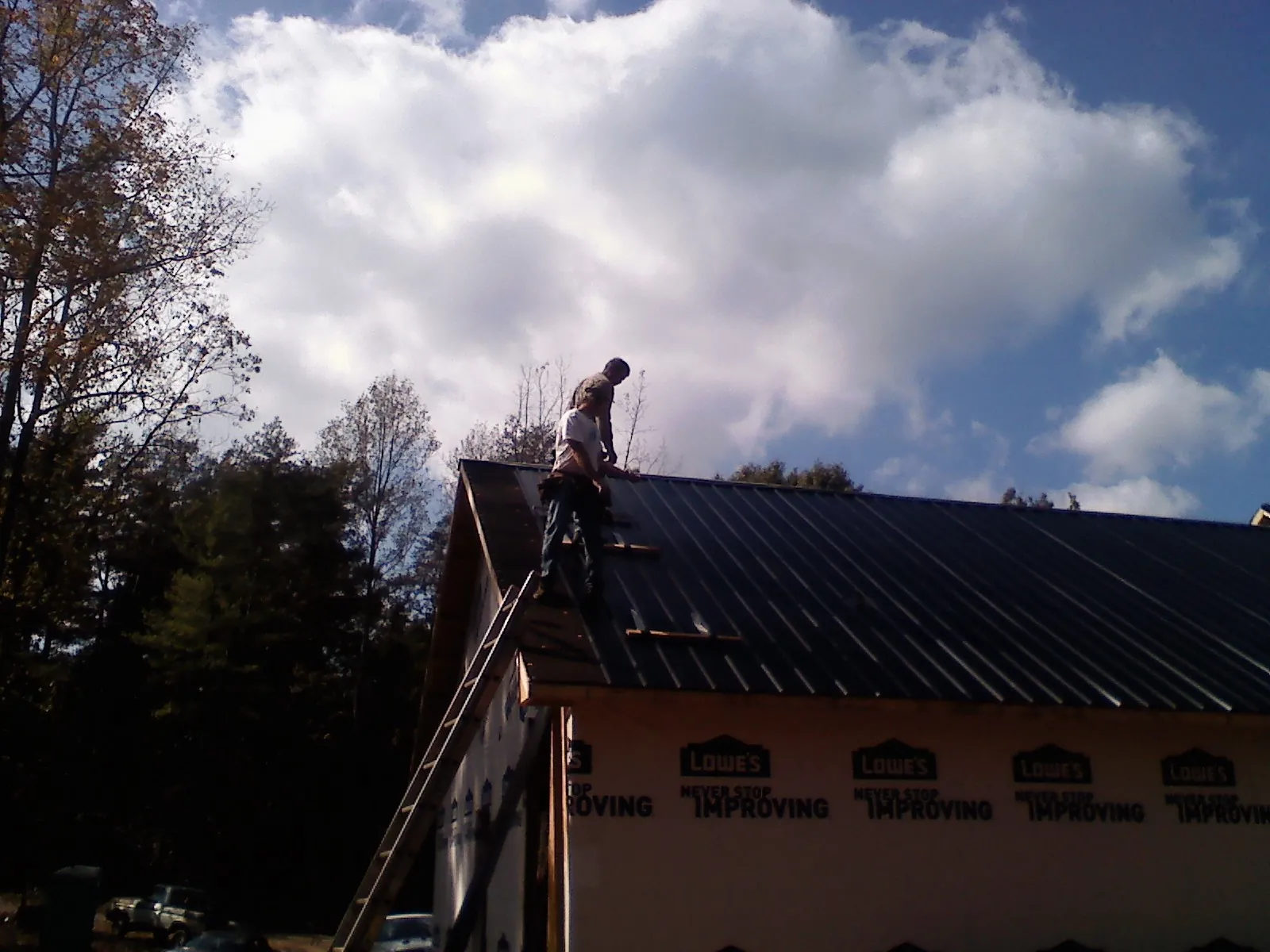 Roofer fastening dark metal panels high against a cloudy sky, from a Roof Inspection job in Wausau