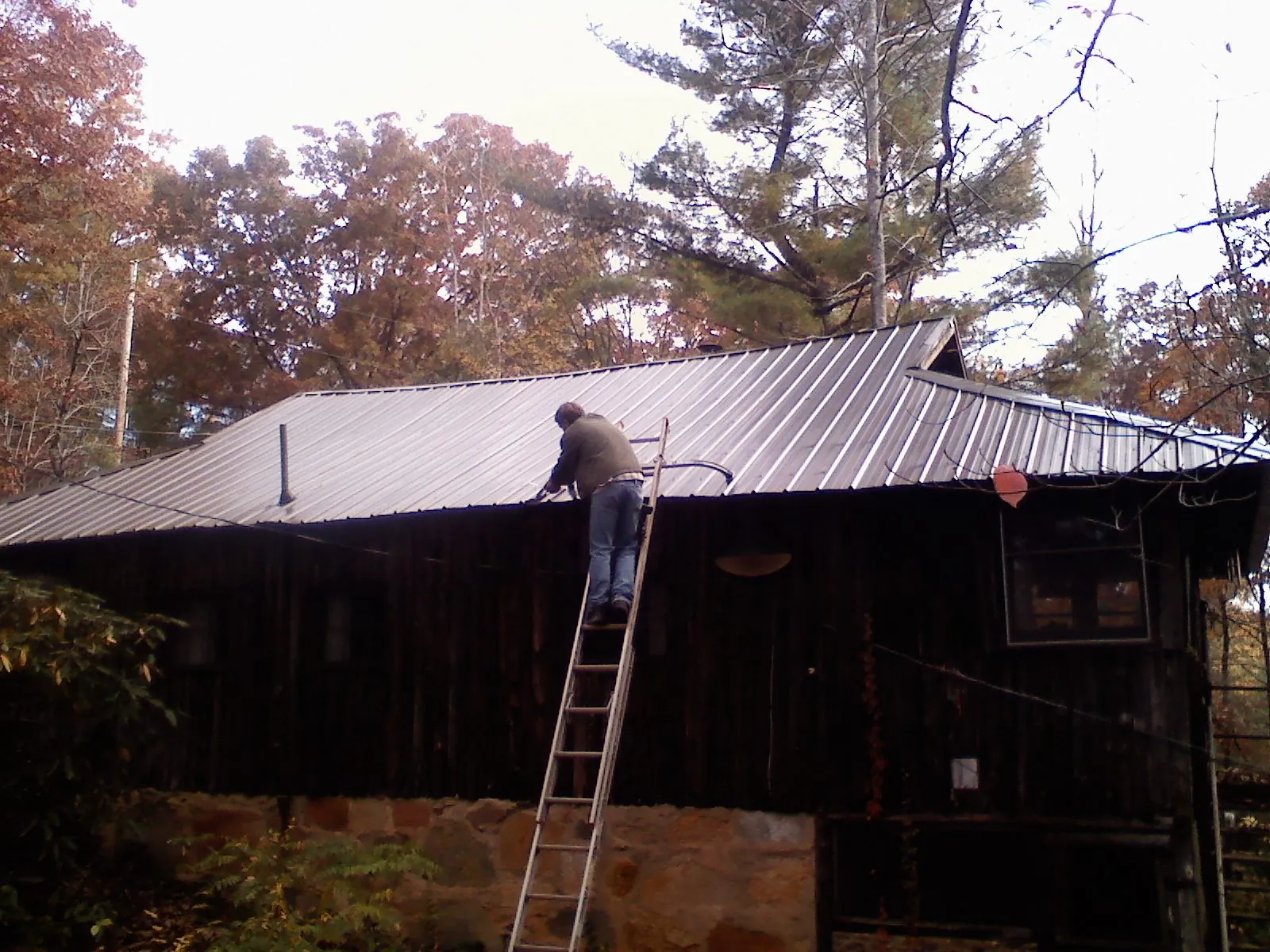 Roofer on a ladder working along the edge of a cabin metal roof in Wausau