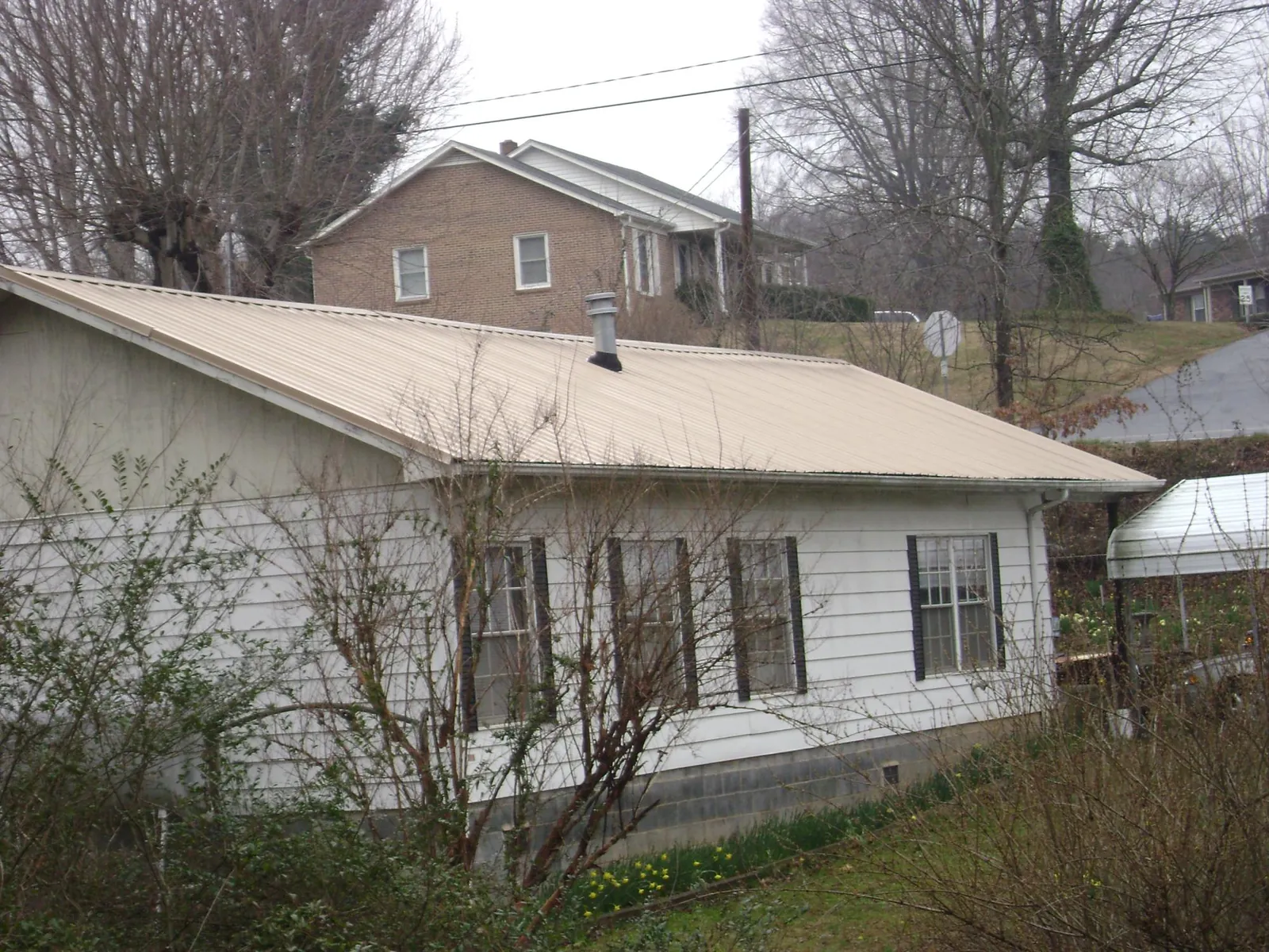 Tan metal roof on a white sided house set into a hillside — Commercial Roofing by Roofing Brothers in Wausau